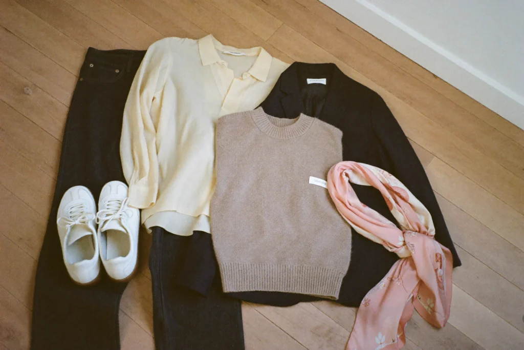 Abgestimmte Kleidungsstücke einer Grundausstattung als Flatlay: Jeans, Bluse, Blazer, Strickpullover, Sneaker und Seidentuch